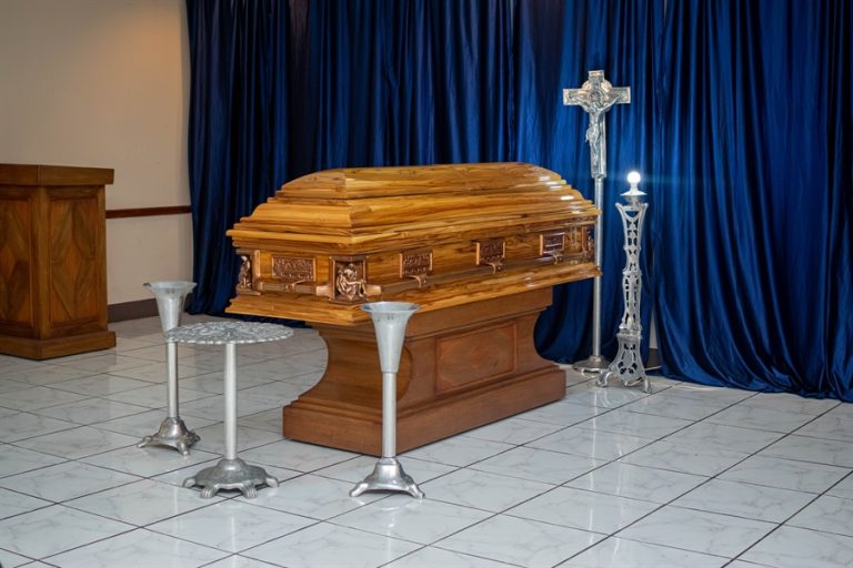 Ataúd con cruz cristiana y cortinas azules en sala de velación de Funeraria El Alba